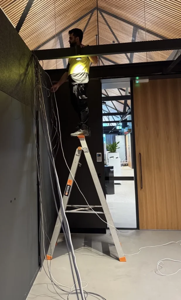 Technician installing security cabling on a ladder in a commercial fit-out