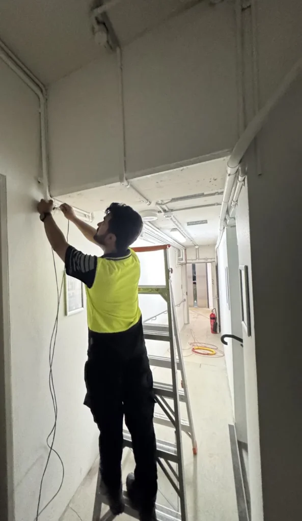 Technician running security cabling along a ceiling in a commercial fit-out