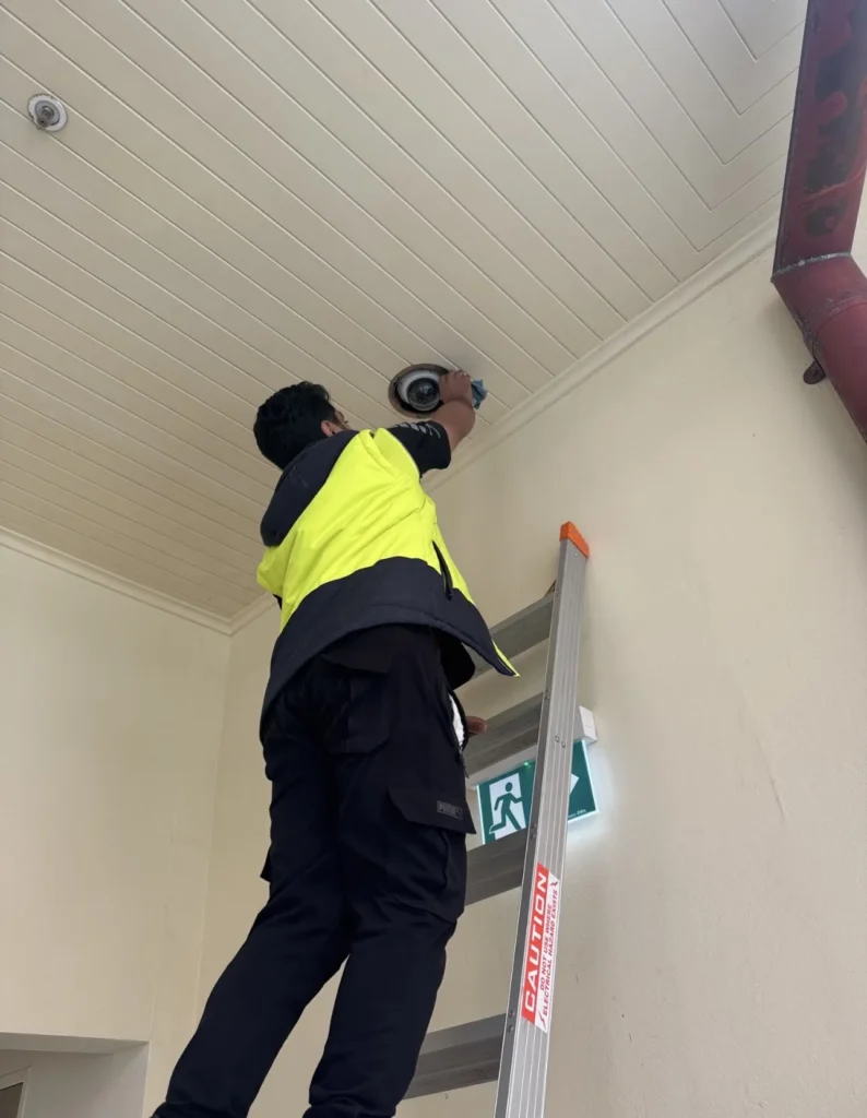 Technician on a ladder mounting a security device with a level